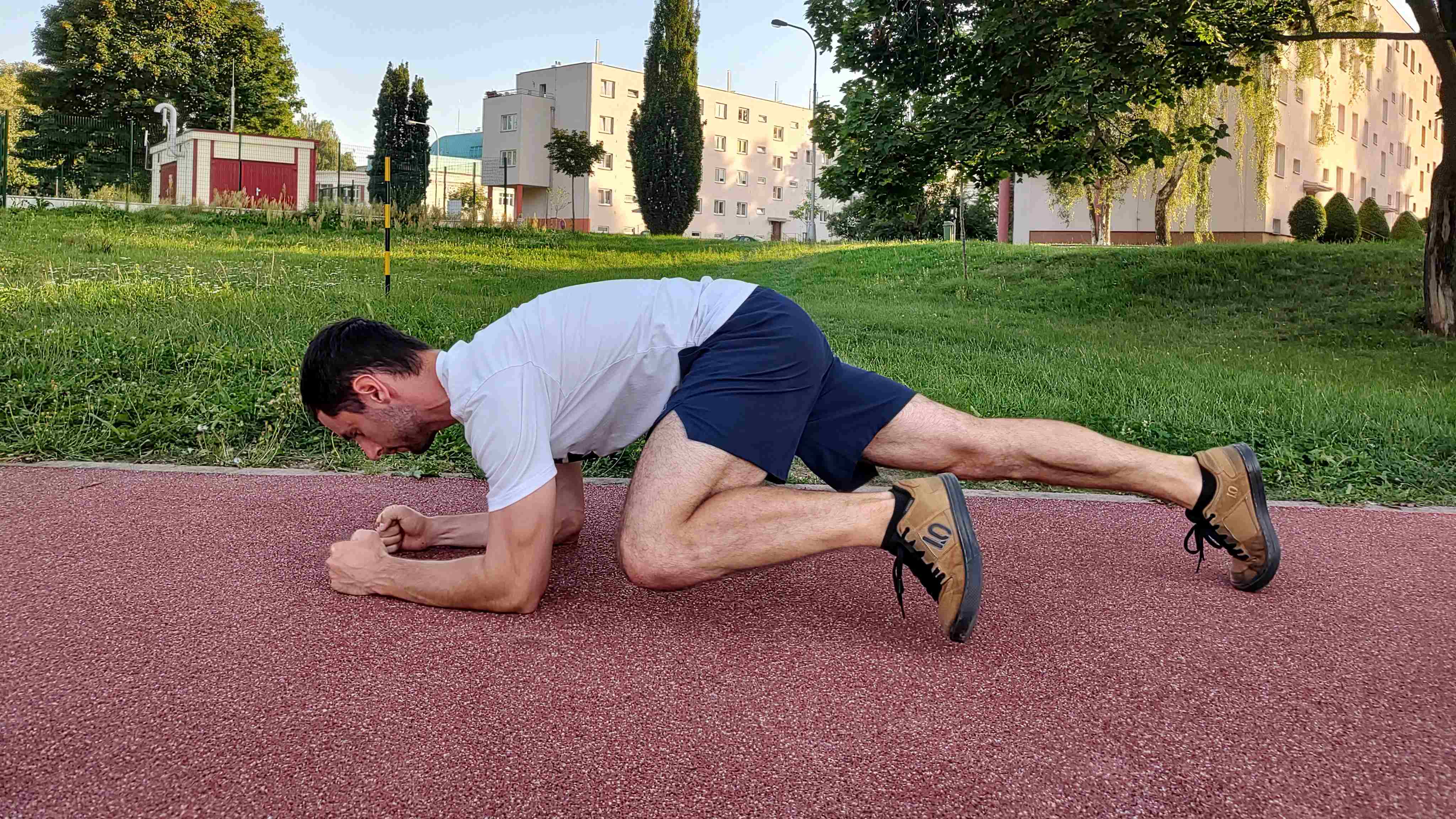 Muž v parku cvičí plank a přitahuje koleno k lokti.